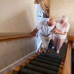 Senior woman helping husband (80s) climb staircase.