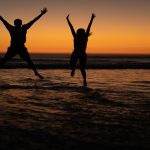 Silhouette of couple jumping together with arms up on the beach